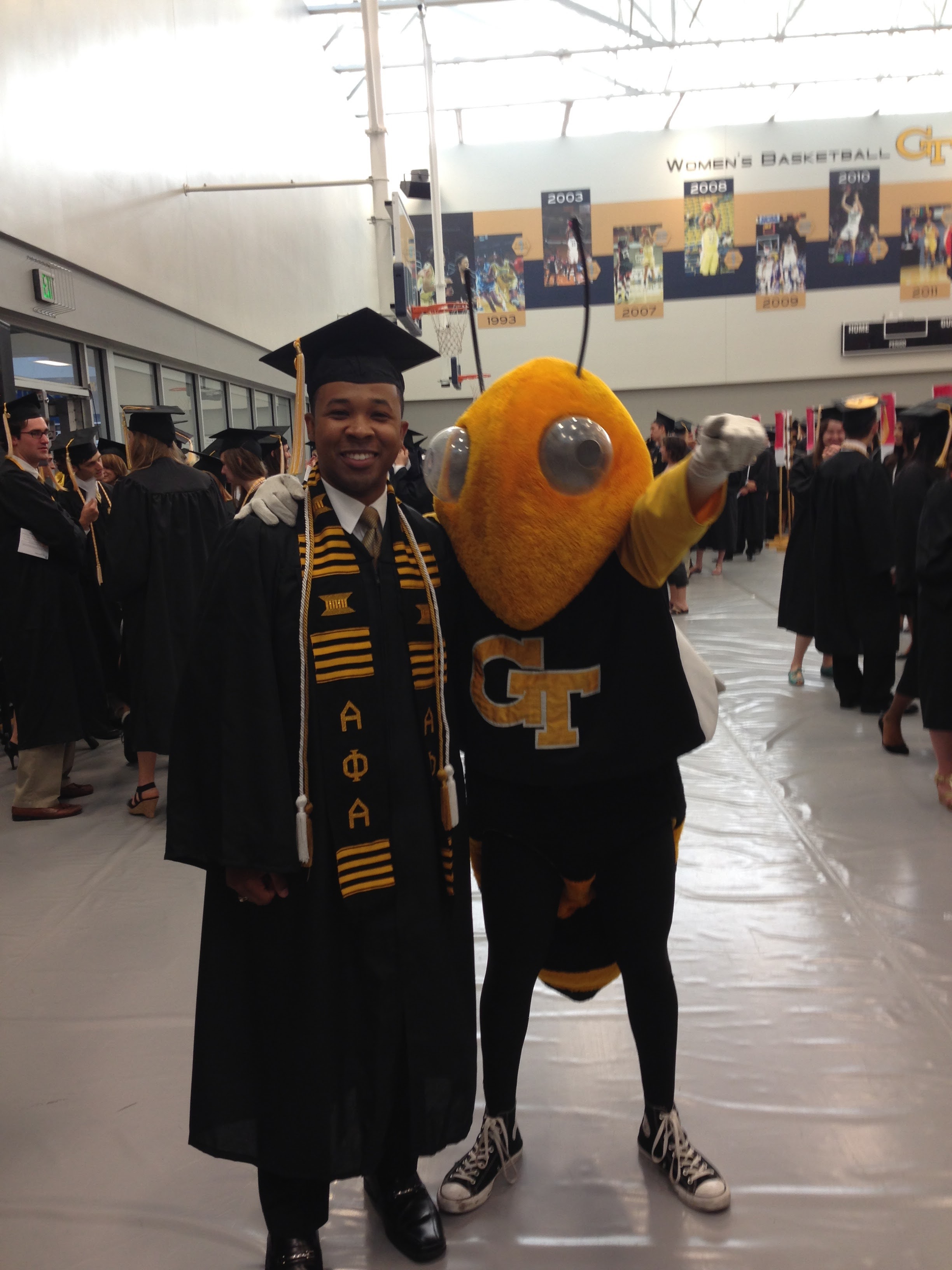 Man in graduation regalia stands with Georgia Tech mascot Buzz.