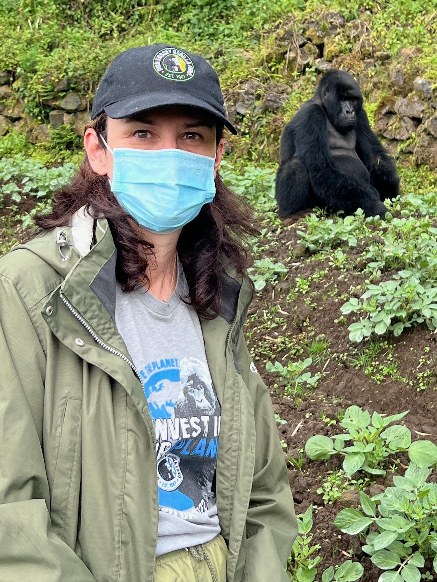 A woman wearing a mask stands near a gorilla.