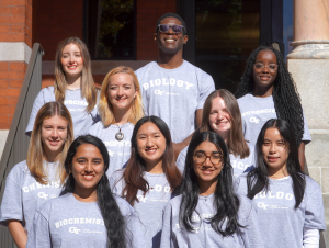 10 students standing in rows in front of brick building.