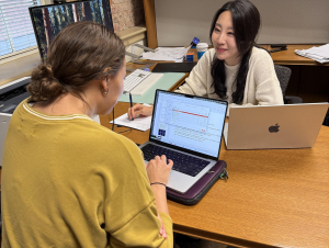 A student and woman confer at a desk.