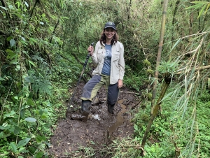 A woman stands in the muddy jungle.